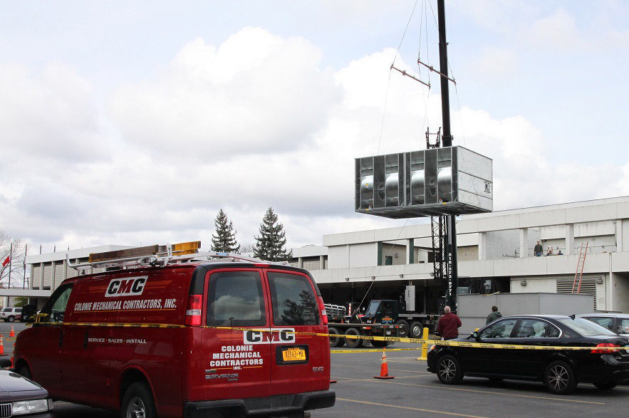 Colonie Mechanical Contractors van outside of a building while an industrial HVAC unit is lifted in to place