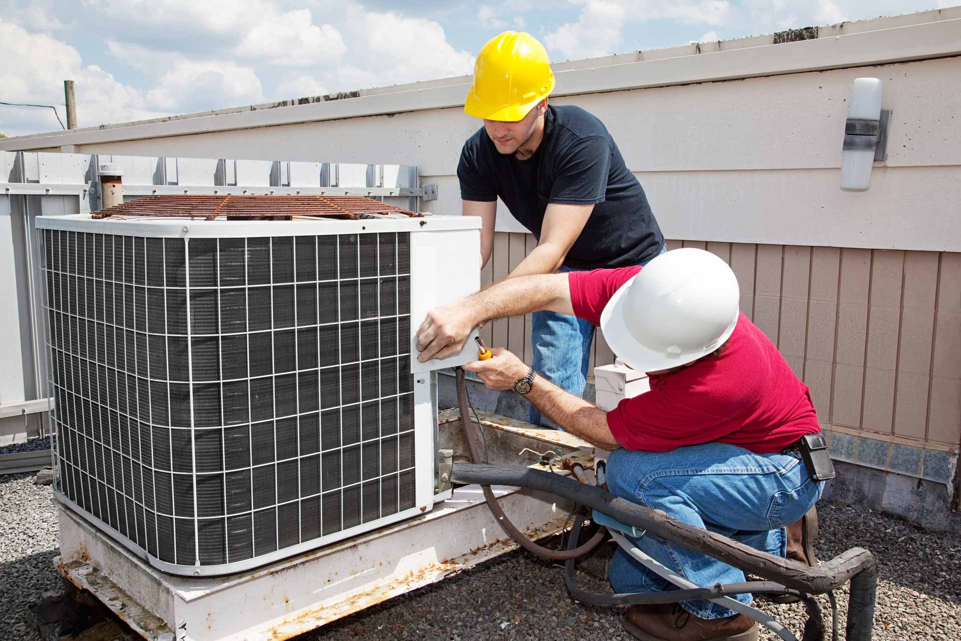 Two workers on the roof of a building working on the air conditioning unit